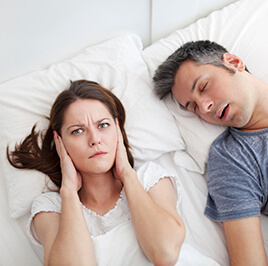 Woman covering ears next to snoring husband